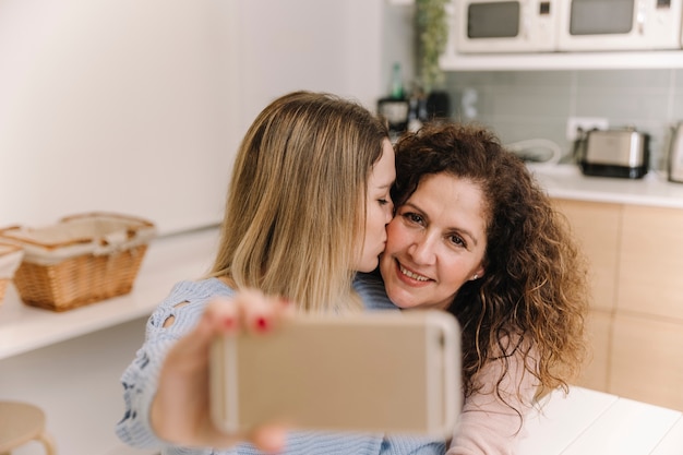 Free photo daughter kissing mom while taking selfie