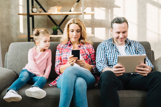 Daughter looking at parents using digital tablet and mobile phone at home