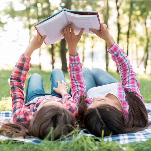 Daughter and mother lying on blanket during reading book in park