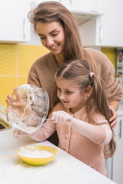 Daughter and mother putting flour in bowl 