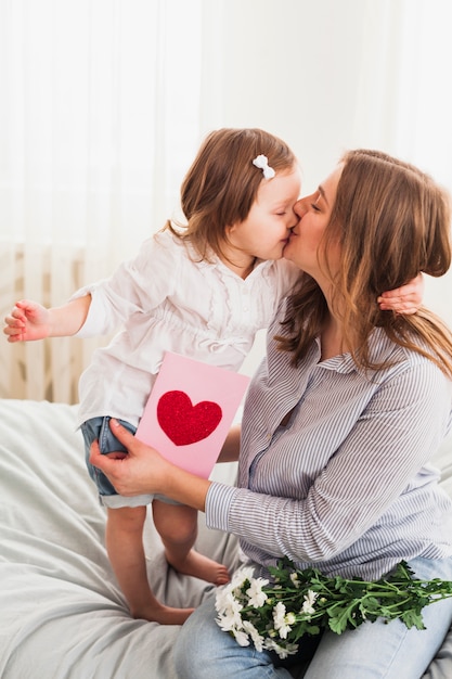 Daughter and mother with greeting card kissing 