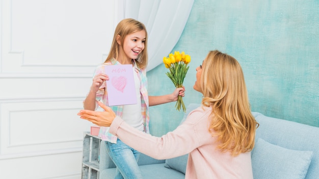 娘の贈り物の花とお母さんのための母の日のはがきを示す