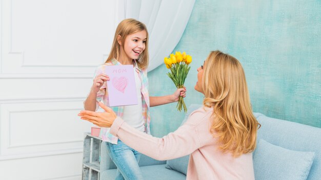 Дочь показывает подарки цветы и открытка ко дню матери для мамы