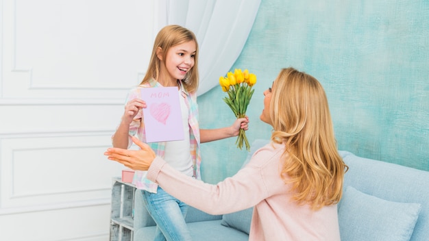 Daughter showing gifts flowers and Mother`s day postcard for mom