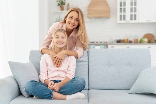Daughter sitting on sofa embraced by her mother