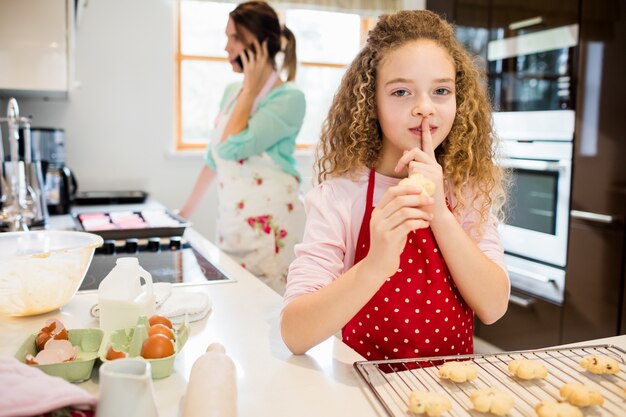 Daughter taking cookies secretly while mother talking on mobile