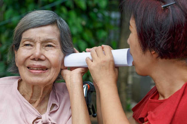Дочь разговаривает с пожилой женщиной с нарушениями слуха, используя бумажную трубку Premium Фотографии