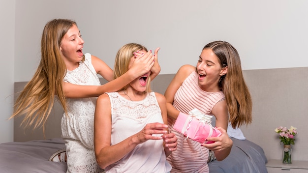 Daughters giving gift box to amazed mother