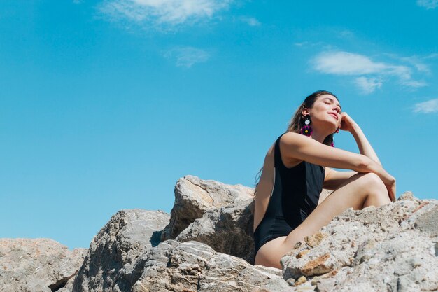 Day dreaming young woman closing her eyes and sitting on rock
