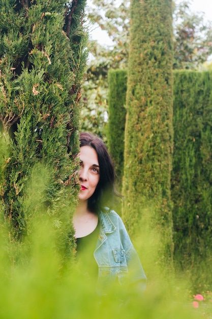 Day dreaming young woman peeking through hedge