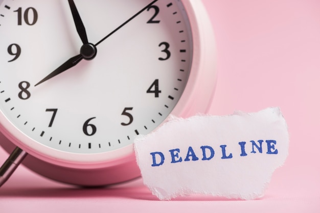 Deadline text on torn paper near the clock against pink background