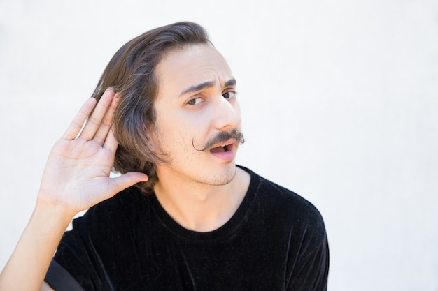 Deaf man with mustache cupping hand behind ear.