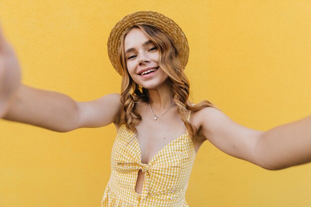 행복 한 미소로 셀카를 만드는 모자에 Debonair 유럽 여자. 자신의 사진을 찍는 물결 모양의 헤어 스타일로 매혹적인 소녀.