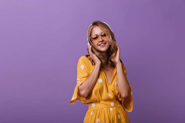 Debonair female model in summer attire enjoying music. Enthusiastic white lady expressing positive emotions on purple.