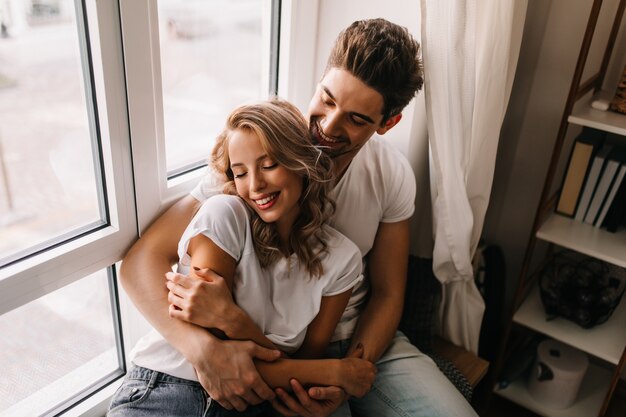 Debonair girl enjoying weekend with boyfriend. Indoor portrait of laughing couple spending morning together.