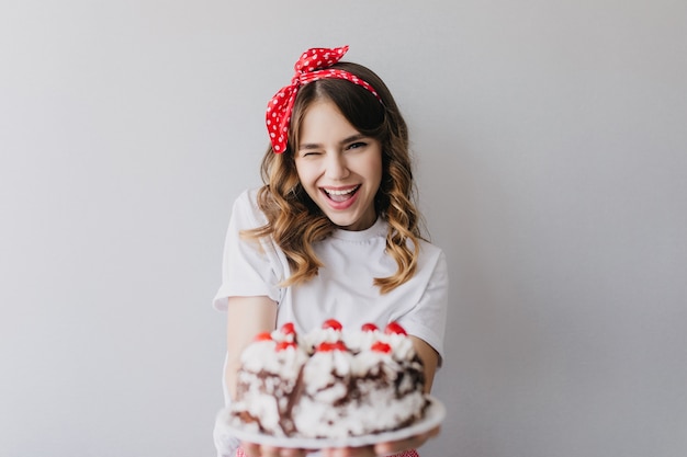 バースデーケーキでポーズをとるロマンチックな髪型のデボネアの女の子。ストロベリーパイを持っている驚くべき笑いの女性。