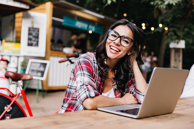 Debonair white girl in casual shirt posing on street with computer. Outdoor portrait of enthusiastic female student using laptop.