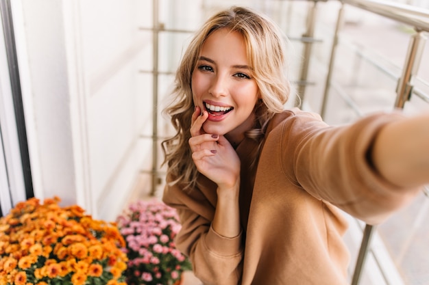 Free photo debonair young woman making selfie at balcony. portrait of smiling dreamy girl posing beside orange flowers.