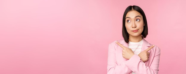 decision concept young asian businesswoman corporate worker pointing fingers sidways two directions showing variants looking indecisive while choosing pink background