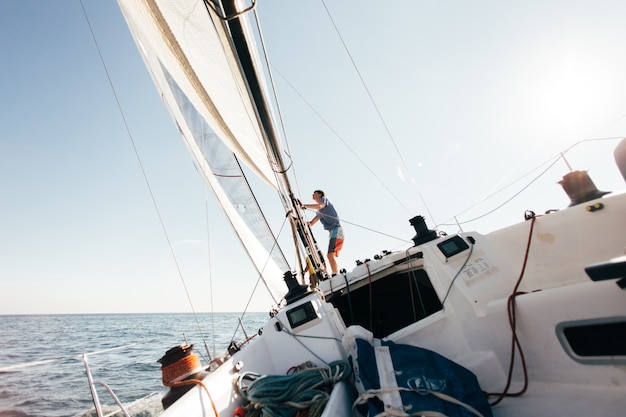 Deck of professional sailboat or racing yacht during competition on sunny and windy summer day, moving fast through waves and water, with spinnaker up