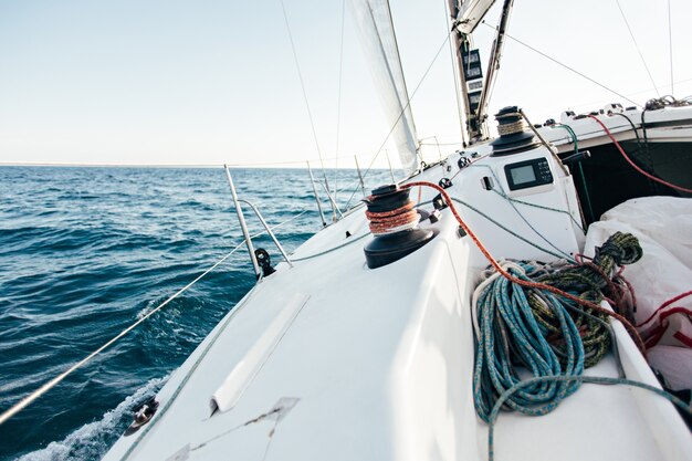 Deck of professional sailboat or racing yacht during competition on sunny and windy summer day, moving fast through waves and water, with spinnaker up