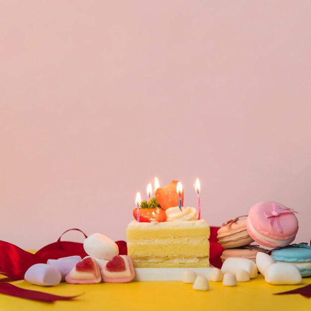 Decorated cakes with candies; marshmallow and macarons on yellow desk
