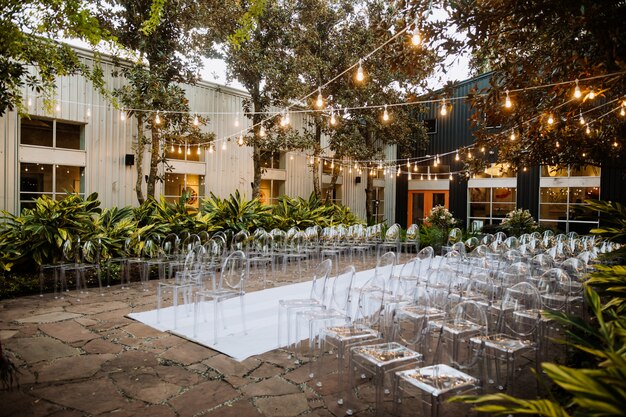 Decorated ceremonial area outdoors with modern transparent chairs and beautiful festoon with lots of trees and plants