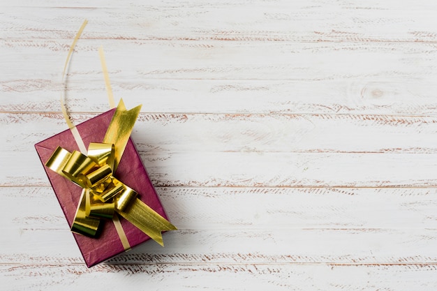 Decorated gift box with golden ribbon on textured white wooden surface