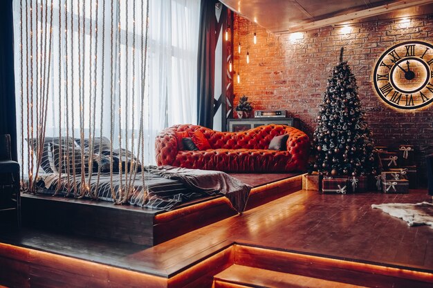 크리스마스 인테리어 장식. 현대 비싼 소파와 로마 숫자와 함께 큰 시계 근처 아름 다운 크리스마스 트리.
