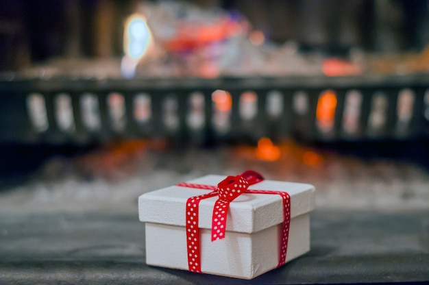 Free photo decorated present with ribbon by the warm cozy fireside. closeup image of  gift box on wooden table in front of burning fireplace