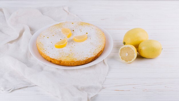Decorated round lemon cake served in plate with lemons on cloth