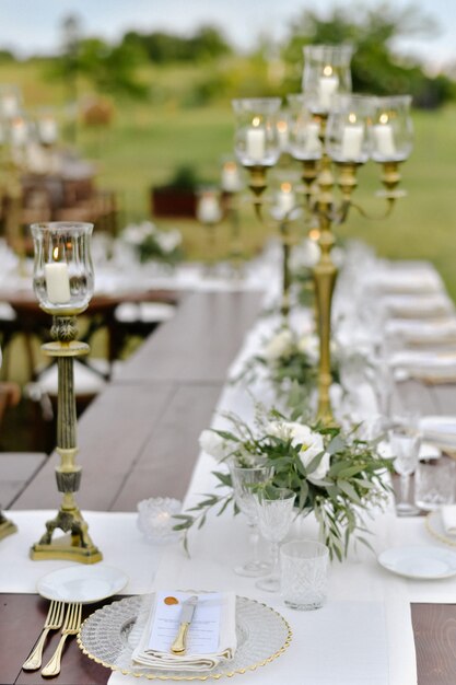 Decorated wedding celebration table with guests seats outdoors in the gardens with burning candles