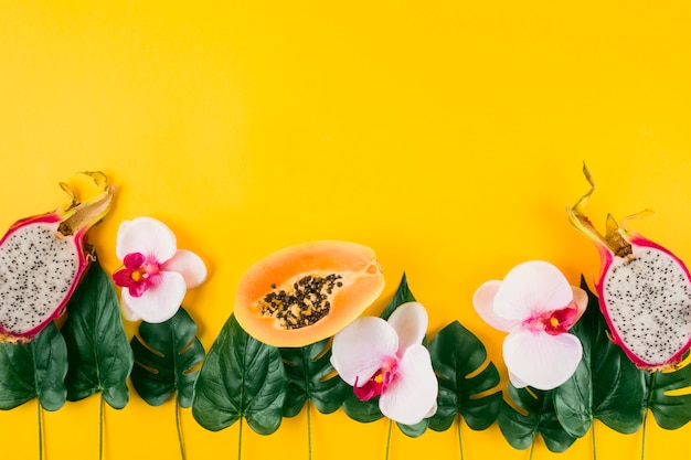 Free photo decoration made with papaya; dragon fruits; orchid and artificial leaves on yellow background