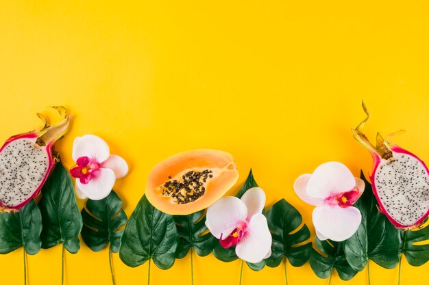 Decoration made with papaya; dragon fruits; orchid and artificial leaves on yellow background