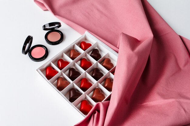 Decorative cosmetics and chocolate over white surface