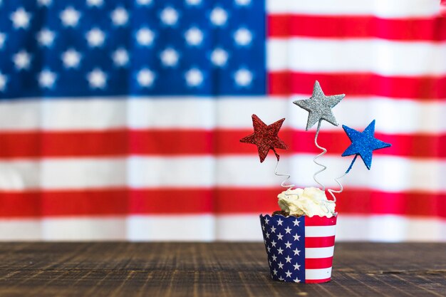 Decorative cupcakes with red; silver and blue stars on wooden desk against american flags for the 4th of july