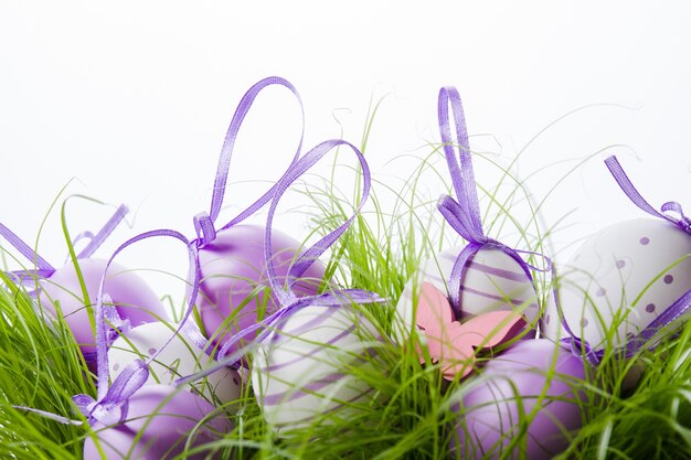 Декоративные пасхальные яйца с фиолетовой лентой на траве