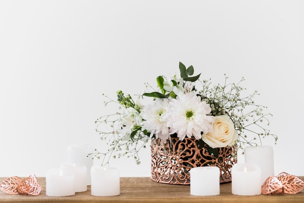 Decorative flower vase with white candles on wooden table against white background