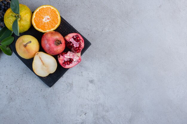 Decorative leaves with sliced and whole pears, pomegranates and tangerines on a black board on marble background. 