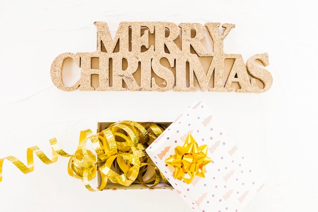 Decorative merry Christmas inscription near gift box with ribbon