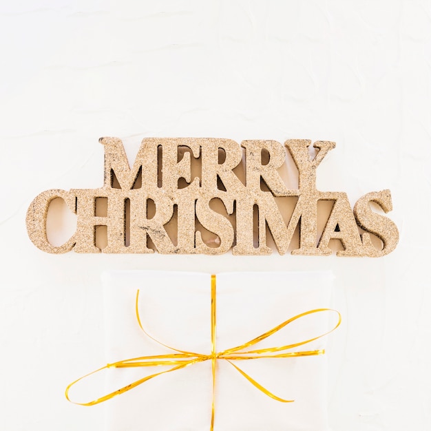 Decorative merry Christmas inscription near gift box in wrap 