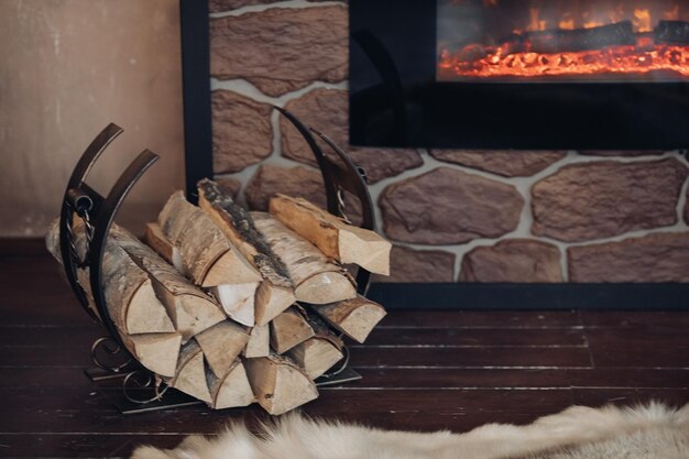 Free photo decorative metallic holder with heap of wooden logs next to stony fireplace with burning logs.