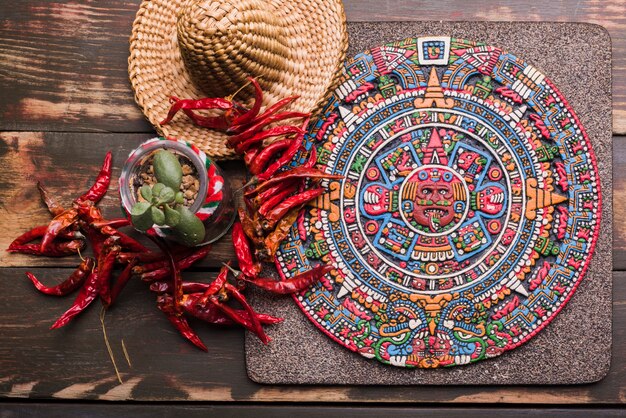 Decorative Mexican symbol on board near dried chili and sombrero