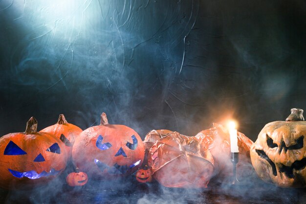 Decorative pumpkins in Halloween style and burning candle and smoke