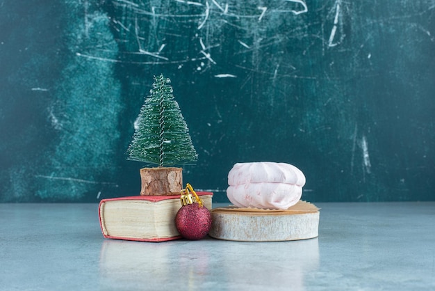 Decorative setup of a bauble, a tree figurine on a small book and stacked cookies on marble.