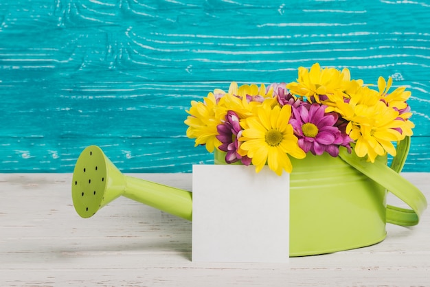 Decorative watering can with flowers and piece of paper