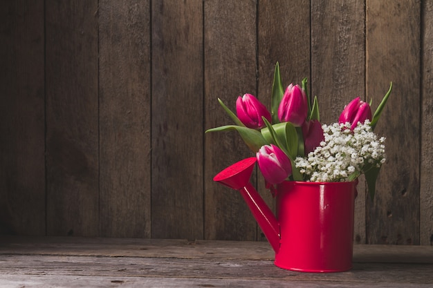 Annaffiatoio decorativo con i fiori sul tavolo in legno