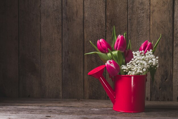 Decorative watering can with flowers on wooden table