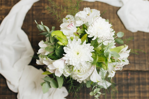 Decorative white flower bouquet with scarf on wooden table