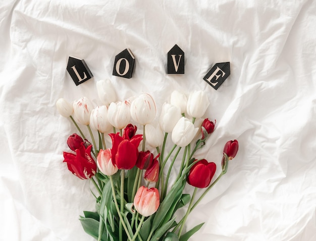 Decorative word love and tulips in a white bed top view